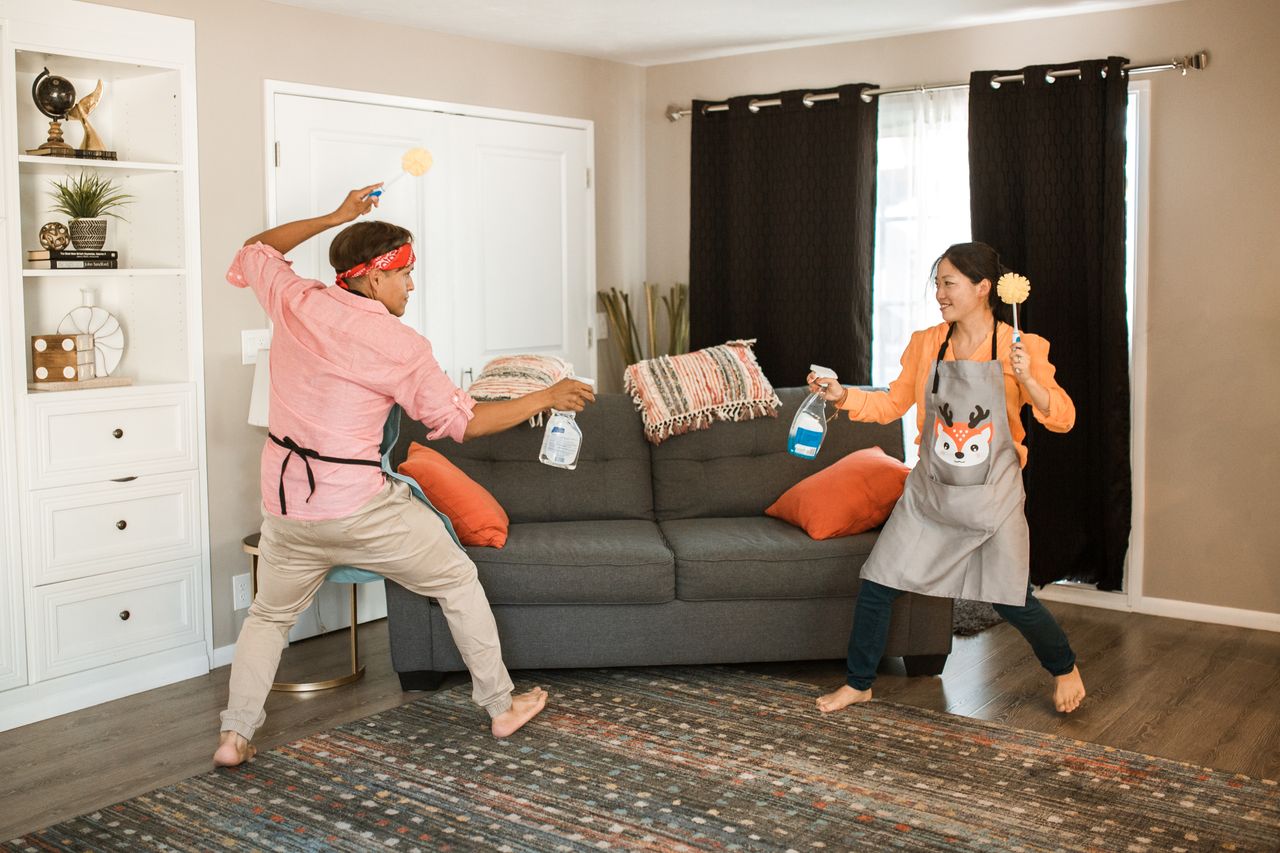 A happy couple is having a playful cleaning battle in their living room, highlighting a carefree home life.